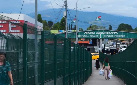 Abhazya Cumhuriyeti tabelasının bulunduğu sınır kapısına doğru yürüyen insanlar
