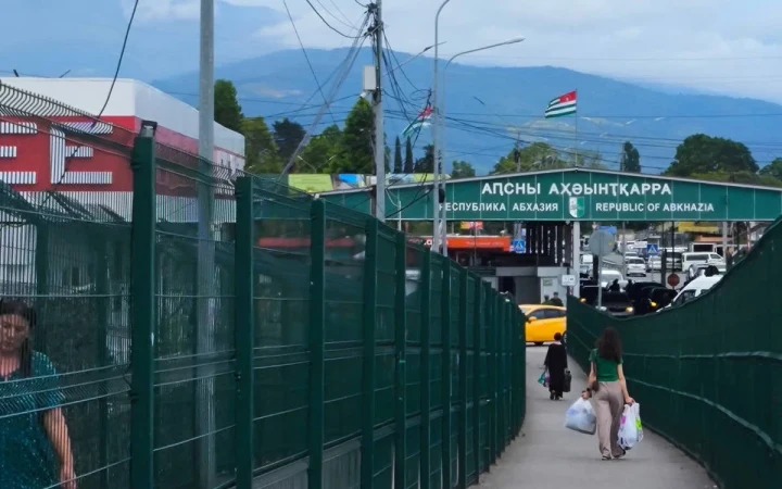 Abhazya Cumhuriyeti tabelasının bulunduğu sınır kapısına doğru yürüyen insanlar
