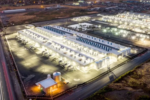 Gece ışıklandırılmış geniş bir veri merkezi kompleksi ve çevresindeki altyapı