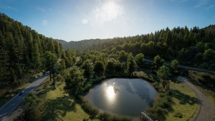 Assetto Corsa EVO’da ağaçlarla çevrili bir göletin ve Eifel yollarının havadan görünümü