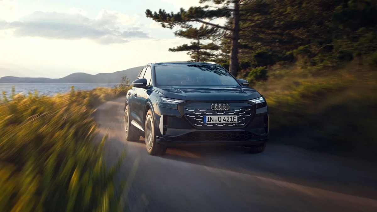 Koyu renkli Audi Q4 e-tron, ağaçlarla çevrili bir yolda ilerliyor.