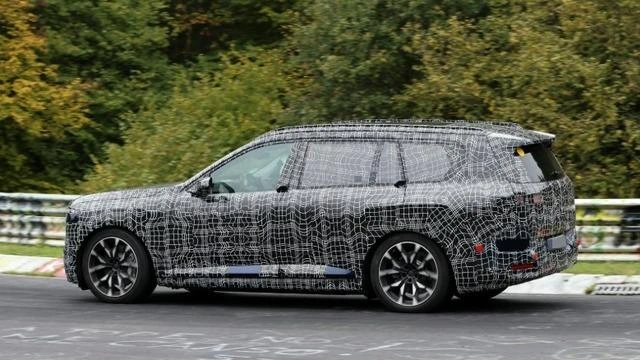 Kamuflajlı BMW iX7 test aracı pistte yandan görüntüleniyor