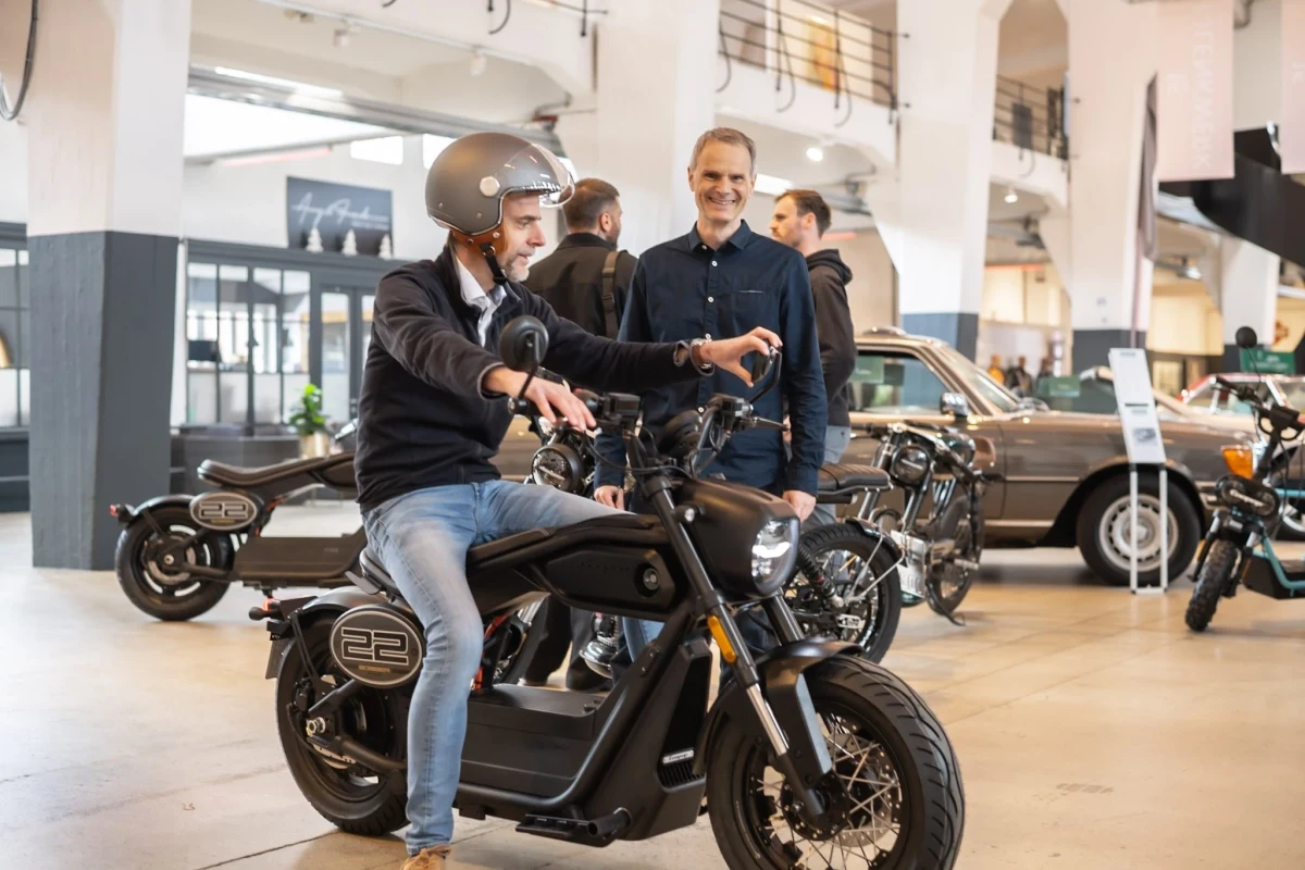 Bir kişinin Coopop Bobber motosiklet üzerinde oturduğu showroom görüntüsü