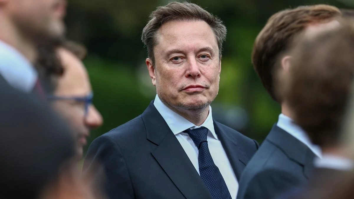 Elon Musk, takım elbiseyle açık havada kalabalık arasında görülüyor.
