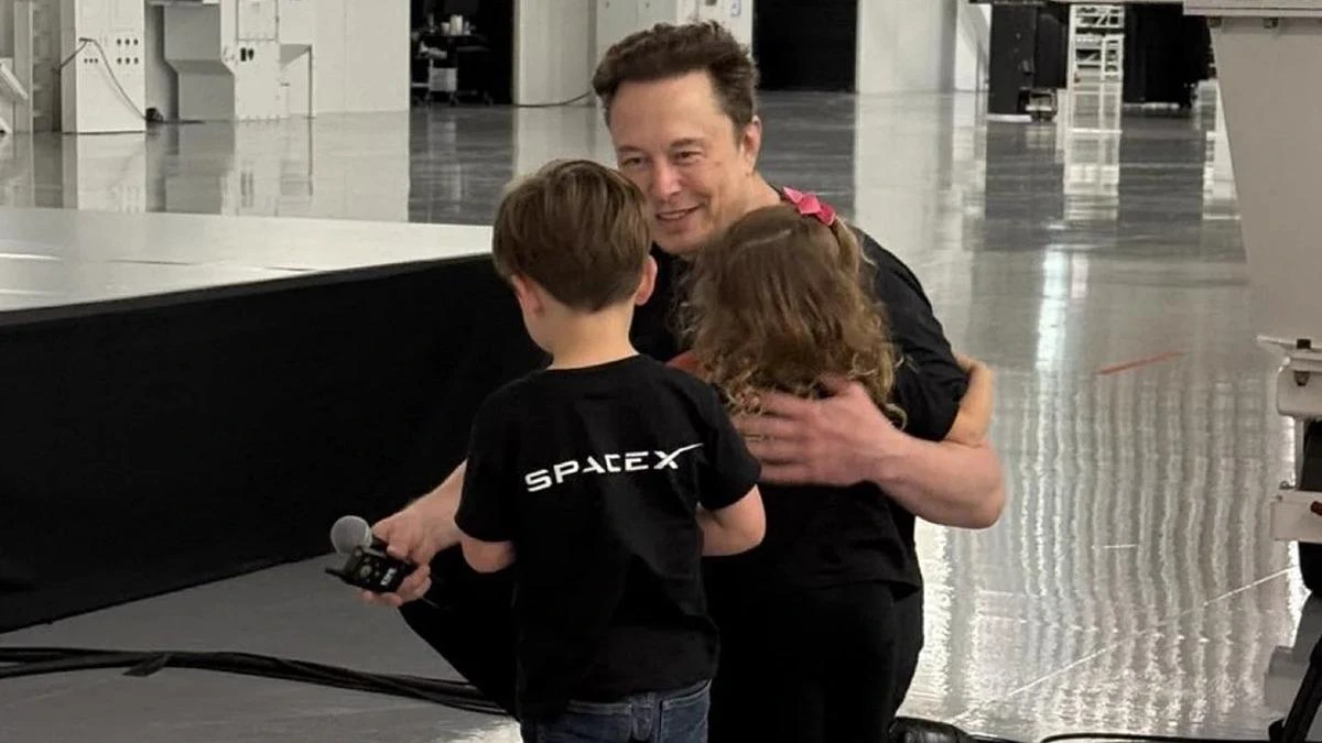 Elon Musk, SpaceX logolu tişört giyen iki çocukla birlikte görülüyor.