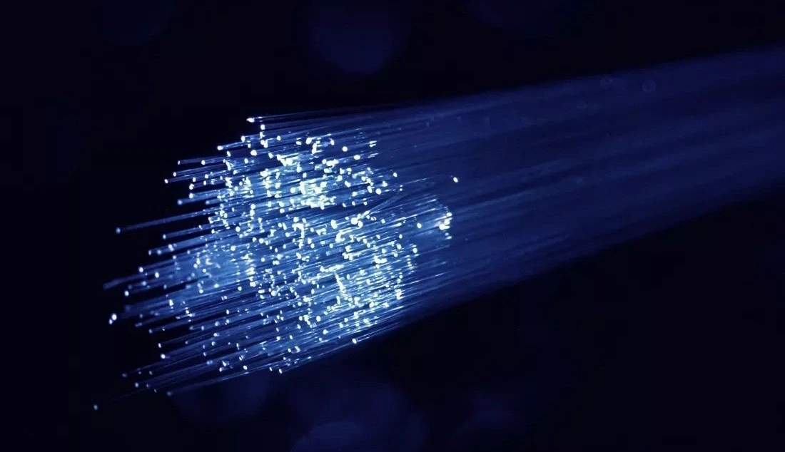Karanlık arka planda ışık saçan fiber optik kablo demeti