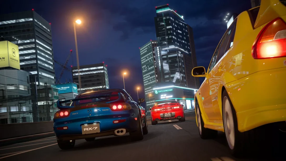 Gece şehir caddesinde yarışan otomobiller; önde mavi ve sarı araçlar görülüyor.