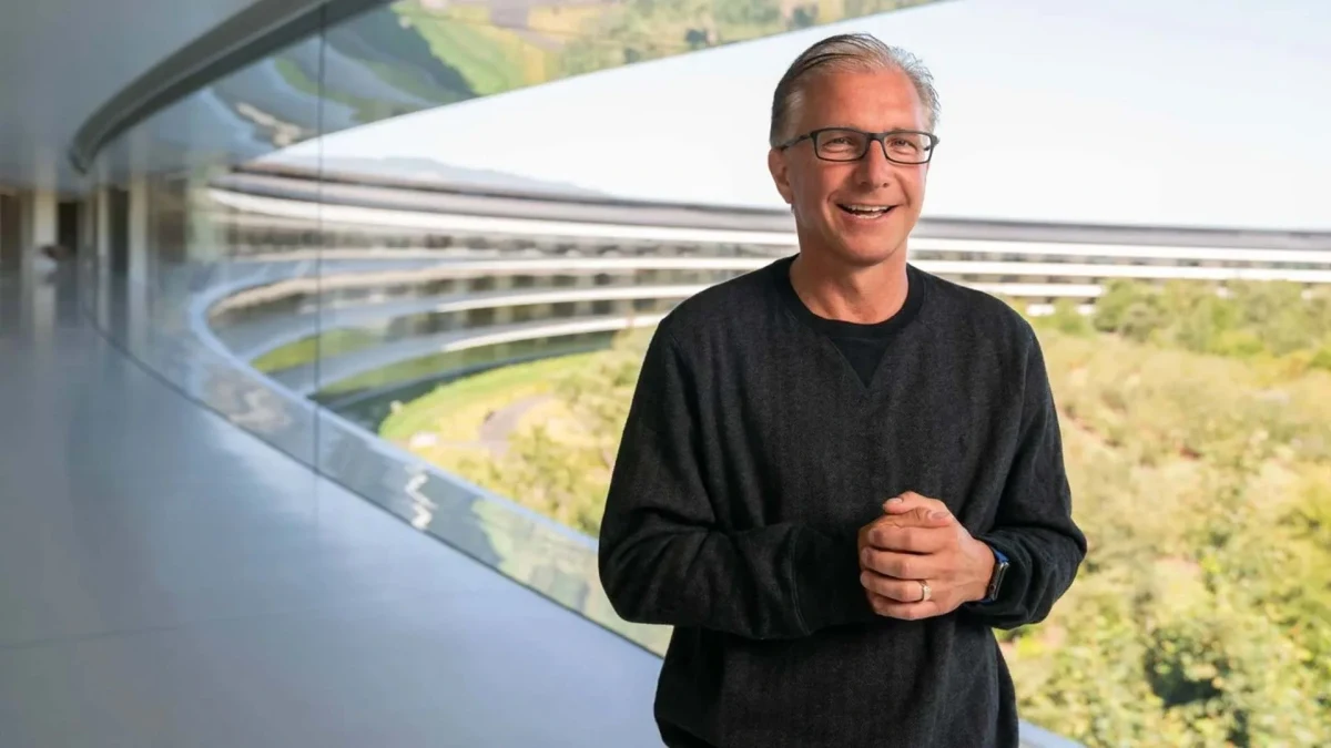Apple yöneticisi Greg Joswiak, modern bir binanın camlı koridorunda poz veriyor