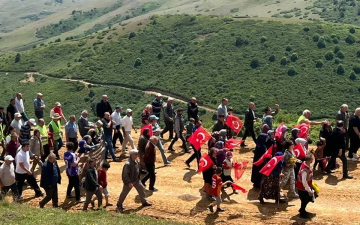 Yeşil bir yamaçta Türk bayrakları taşıyan kalabalık bir grup yürüyor