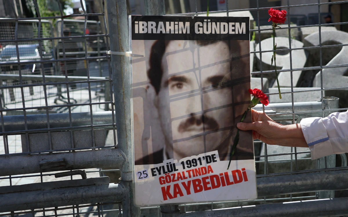İbrahim Gündem’in fotoğrafının ve kaybedildiğine ilişkin yazının yer aldığı afişe bir karanfil uzatılıyor