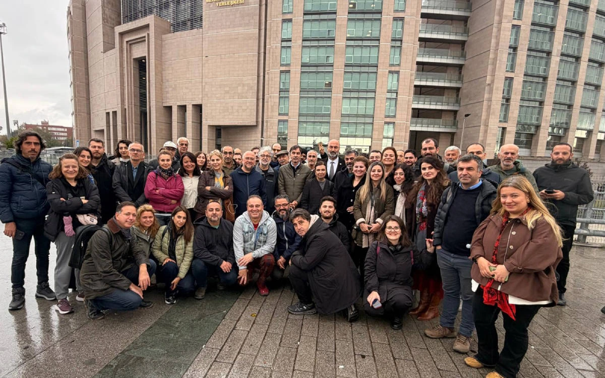 Bir grup gazeteci ve medya çalışanı, büyük bir binanın önünde toplu fotoğraf için poz veriyor.