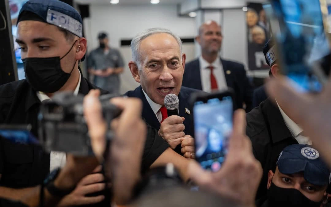Benjamin Netanyahu, kalabalık bir ortamda elinde mikrofonla konuşurken çevresindekiler cep telefonlarıyla görüntü alıyor.
