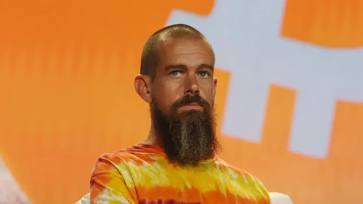 Jack Dorsey, turuncu arka plan önünde renkli tişörtüyle oturuyor.