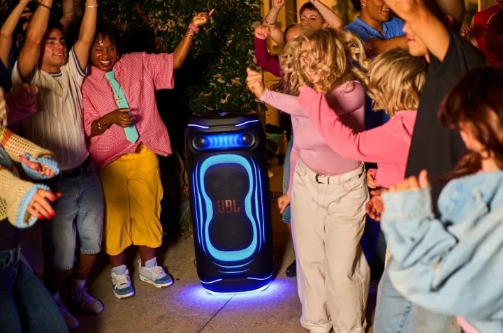 JBL PartyBox hoparlörünün ışıkları açıkken çevresinde dans eden bir grup insan