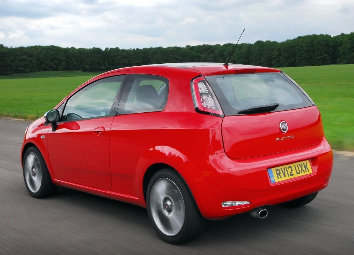 Kırmızı Fiat Punto, arkadan üç çeyrek açıyla yolda ilerliyor.