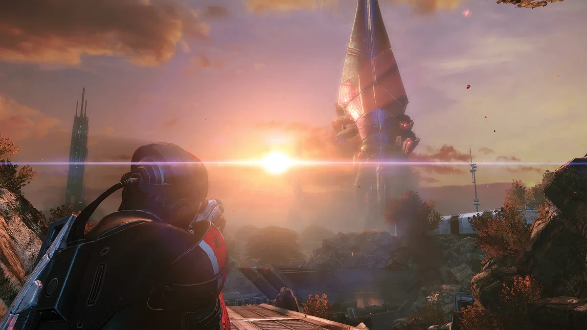 Mass Effect sahnesinde gün batımında uzaktaki büyük yapıya bakan zırhlı karakter