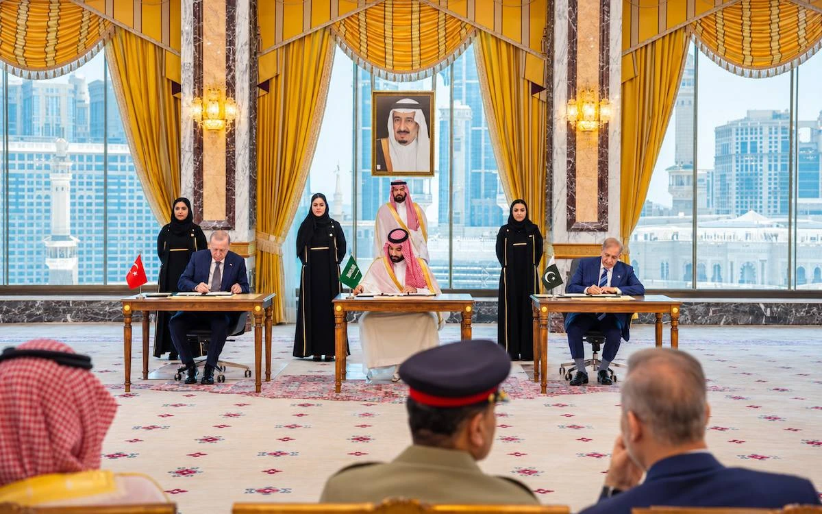 Suudi Arabistan’daki salonda uzun bir masada oturan yetkililer, imza belgelerinin yanında duruyor.