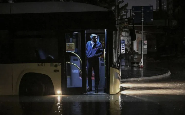 Şiddetli yağmur altında duran otobüsün kapısında bekleyen kişi
