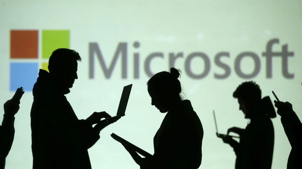 Microsoft logosunun önünde bilgisayar ve tablet kullanan kişilerin silüetleri