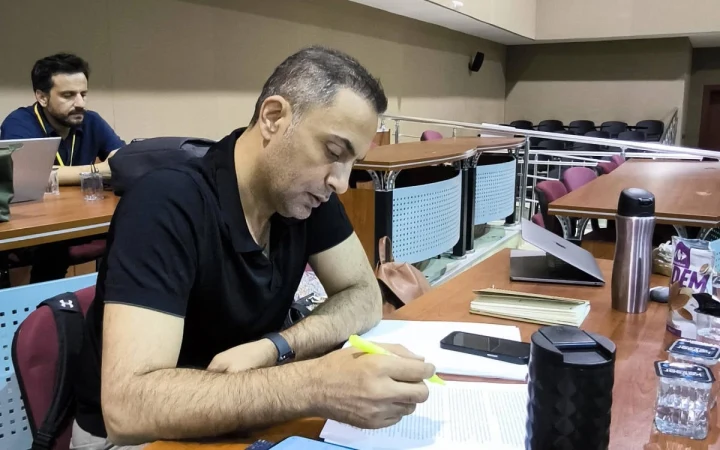 Murat Ağırel bir masada otururken önündeki belgeye not alıyor