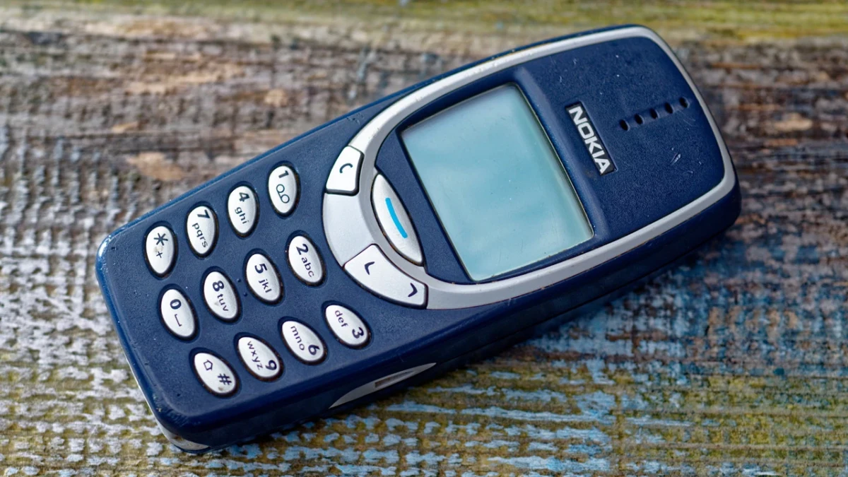 Mavi Nokia 3310 tuşlu telefon, aşınmış ahşap bir yüzey üzerinde duruyor.