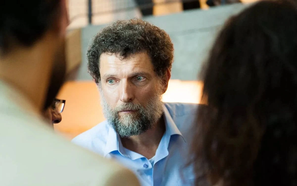 Osman Kavala, iki kişinin arasında otururken görülüyor