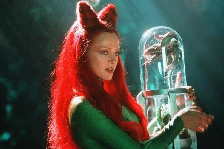 Kırmızı saçlı Poison Ivy karakteri, cam bir fanusun yanındaki bitkiyi tutuyor