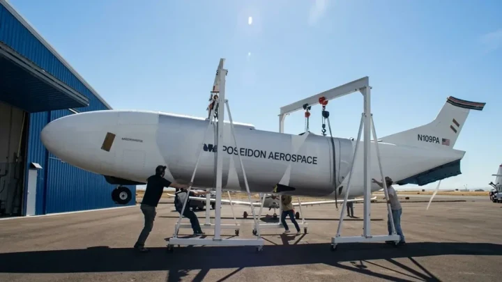 Poseidon Aerospace Egret otonom kargo uçağı, hangar önündeki pist alanında ekipmanlarla desteklenmiş halde duruyor.