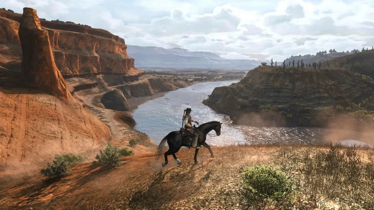 Red Dead Redemption’da at üzerindeki kovboy, nehir ve kayalıklarla çevrili geniş bir manzaraya bakıyor.