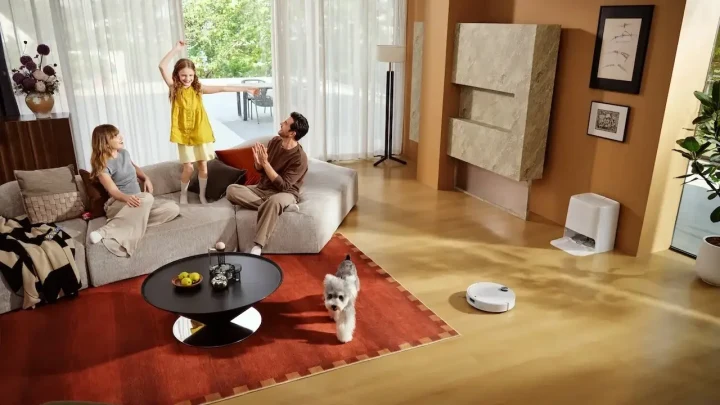 Bir aile ve küçük bir köpek salonda bulunurken robot süpürge zeminde ilerliyor