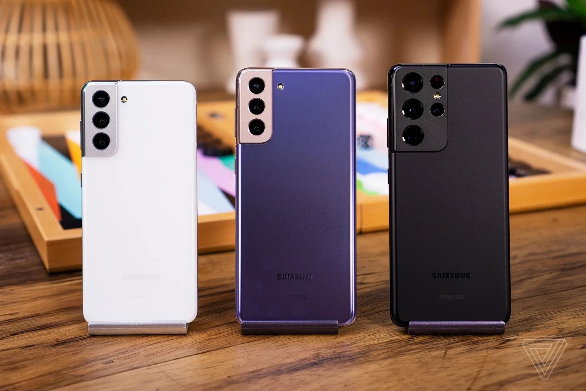 Ahşap masa üzerinde arka yüzleri görünen beyaz, mor ve siyah Samsung Galaxy telefonları