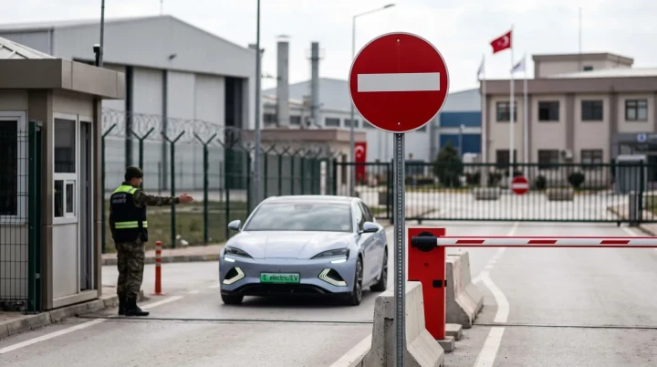 Bir elektrikli otomobil, güvenlik kulübesi ve bariyerin bulunduğu tesis girişinde görülüyor.