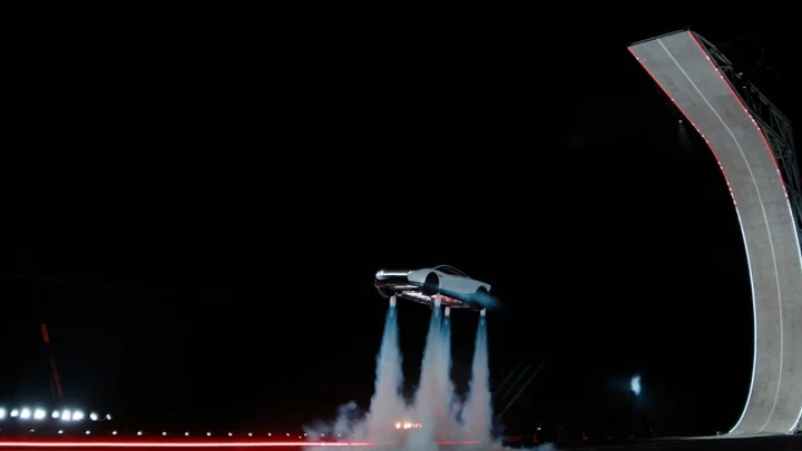 Tesla Roadster, karanlık bir tanıtım alanında iticilerinden çıkan hava akımlarıyla rampanın yanında havada duruyor.