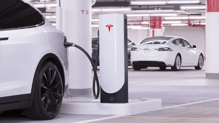 Tesla Supercharger istasyonunda şarj kablosu bağlı beyaz bir Tesla otomobil ve arka planda başka bir Tesla aracı