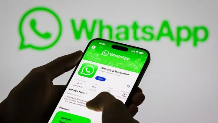 Bir kişi, WhatsApp logosunun önünde tuttuğu akıllı telefonda uygulama sayfasını görüntülüyor.