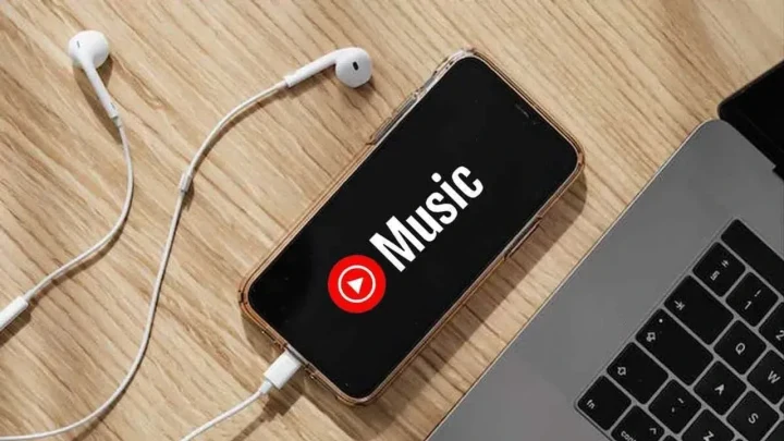 Kulaklık ve dizüstü bilgisayarın yanında, ekranında YouTube Music logosu bulunan telefon