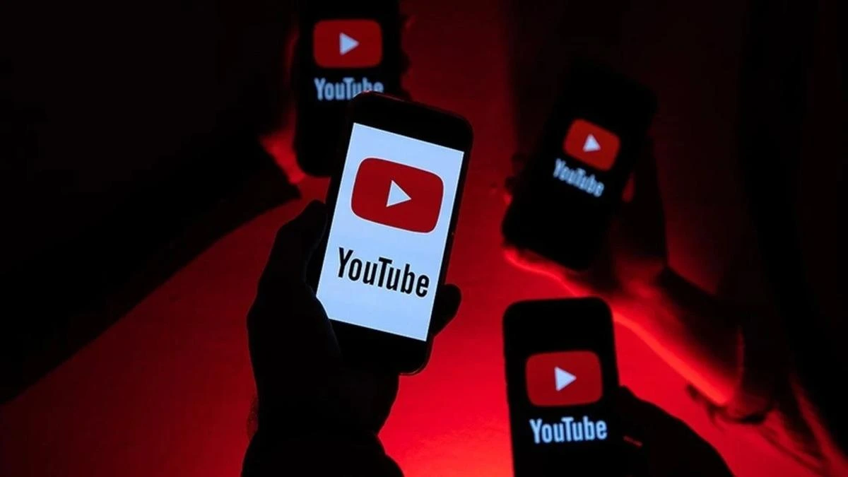 Kırmızı ışık altında YouTube logosu görünen telefonları tutan kişiler